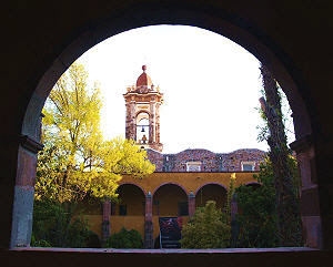 One of the towers of Las Monjas church in San Miguel de Allende, seen through the arches of Bellas Artes art school